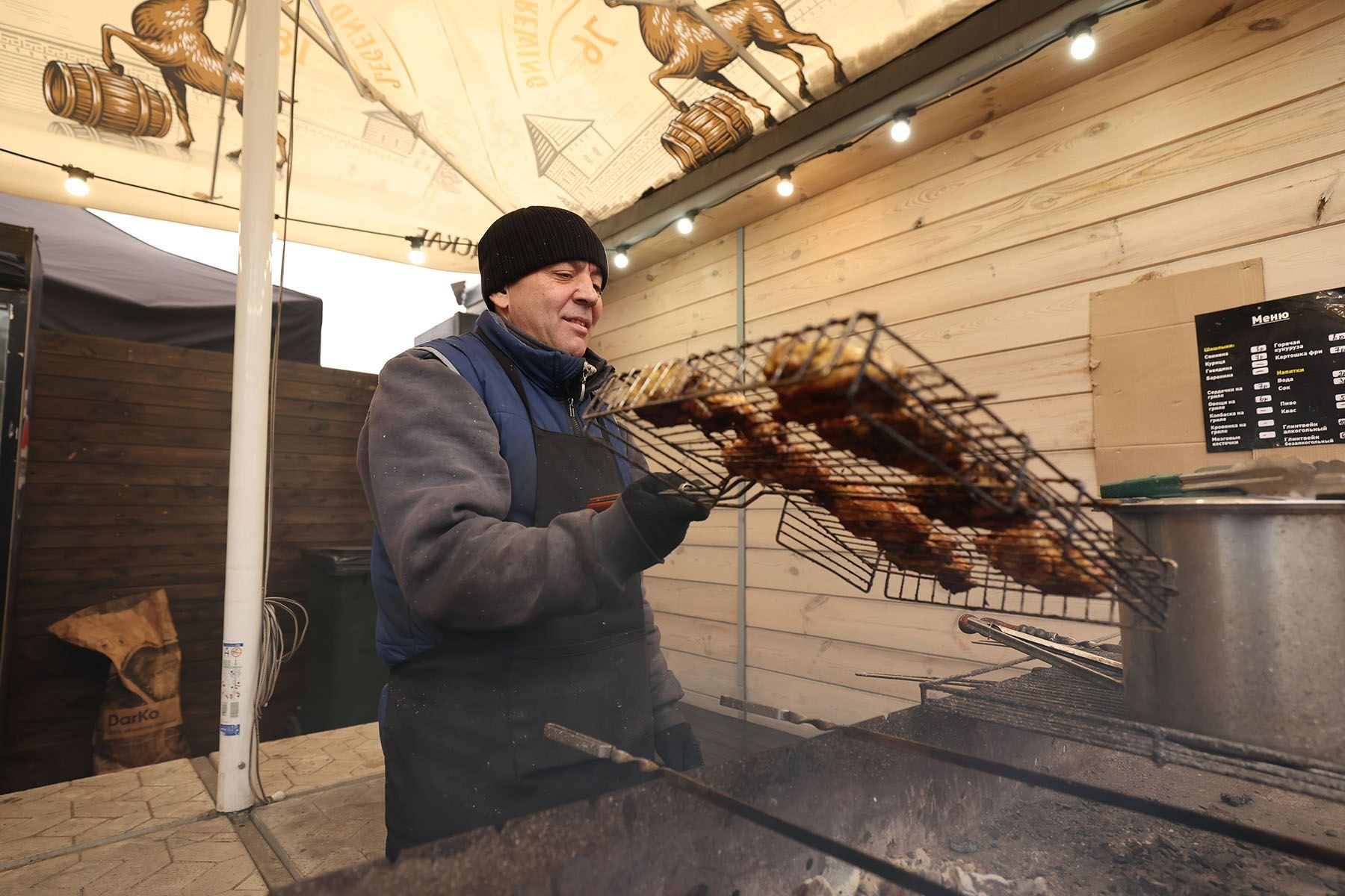 Мужчина готовит мясо на новогодней ярмарке в Минске
